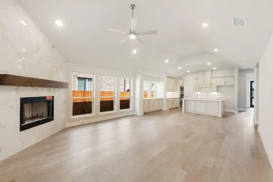 Open living room with marble fireplace, vaulted ceiling, and light hardwood floors open to kitchen