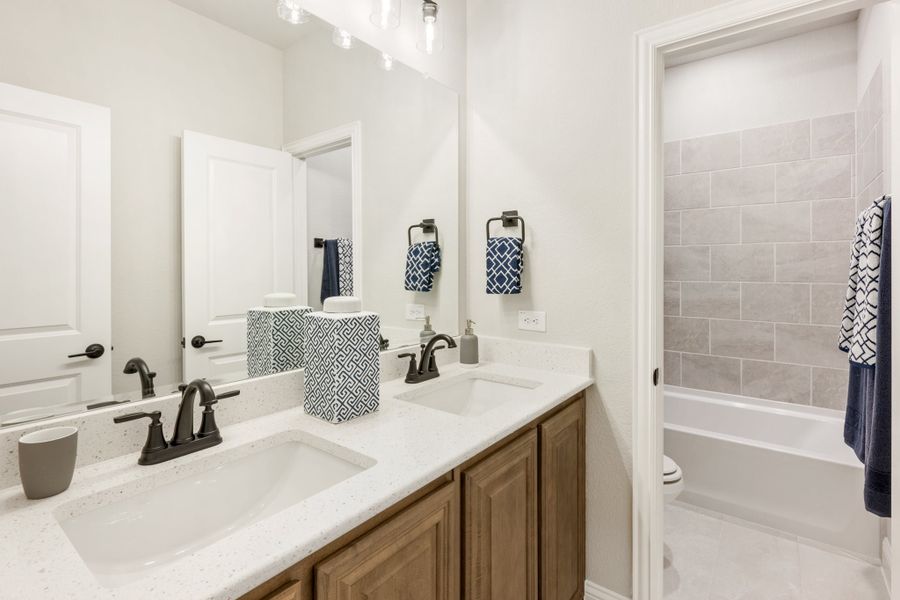 Bathroom with double sink vanity, wood cabinets, white quartz countertop, and tiled shower-tub combo