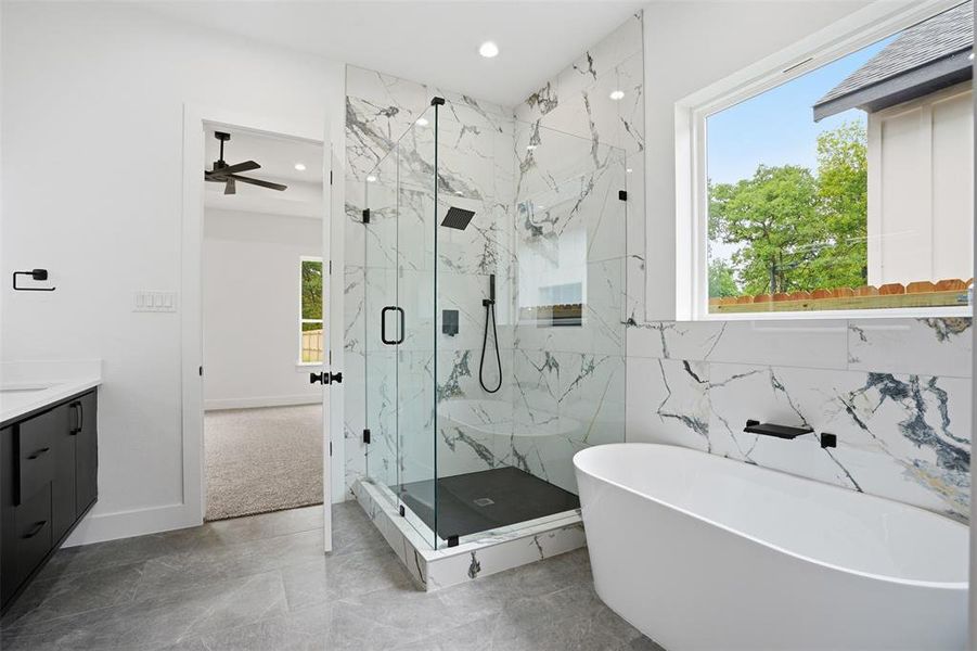 Modern bathroom featuring a freestanding soaking tub, a frameless glass shower enclosure with marble-look tile surround and black fixtures, and a contemporary vanity with a white countertop