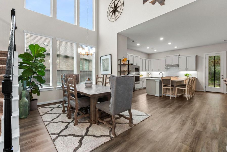 Open-concept living area featuring high ceilings with upper-level windows, wood-finish flooring, and a dining space with a chandelier