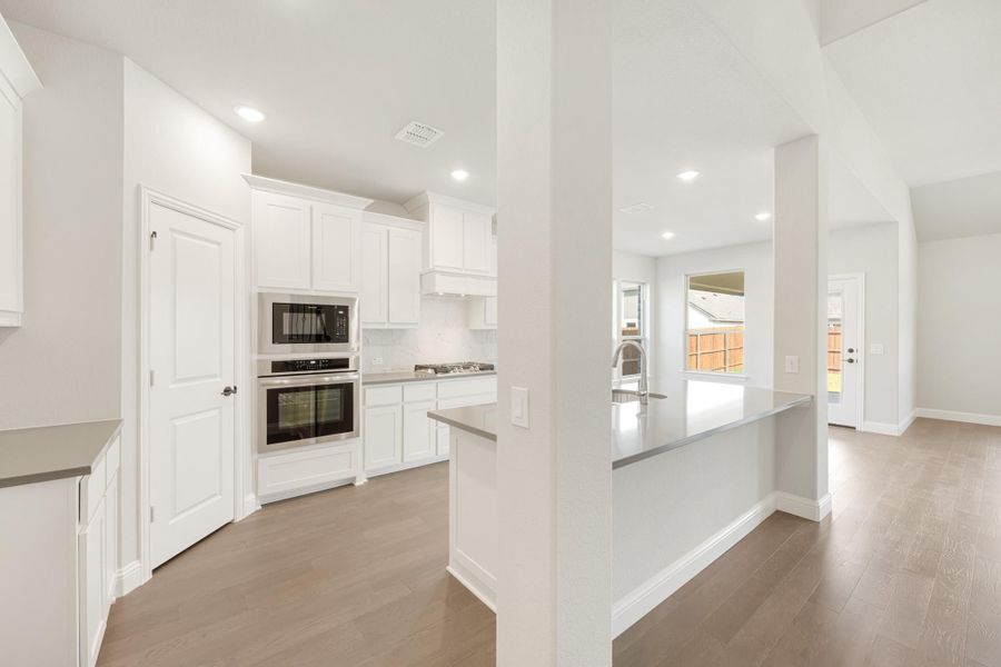 Open kitchen with white cabinets, stainless steel appliances, gray countertops, and wood-look floors