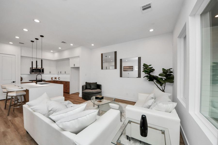 Experience modern elegance in this inviting living room, featuring sleek white walls, a cozy seating area, and seamless flow into a stylish kitchen, perfect for entertaining and relaxing.