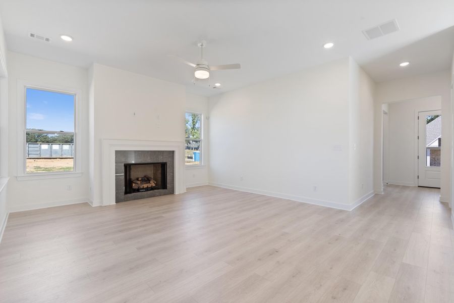 Living area featuring light-toned wood-finish flooring, recessed lighting, a ceiling fan, and a fireplace with a stone-surround mantel Living area featuring light-toned wood-finish flooring, recessed lighting, a ceiling fan, and a fireplace with a stone-surround mantel
