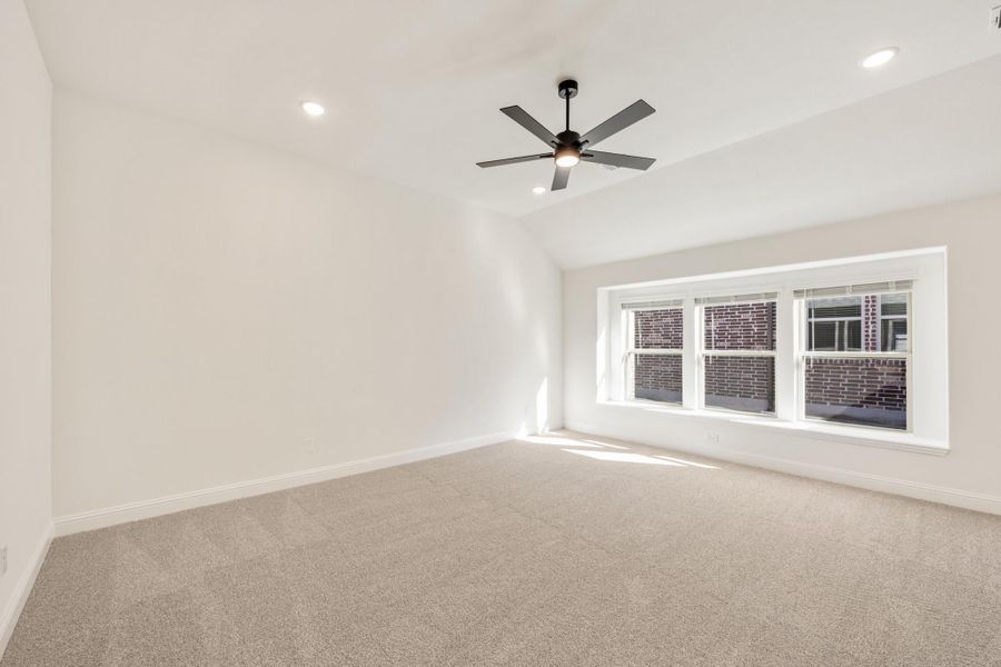 Empty bedroom with vaulted ceiling, ceiling fan, carpet flooring, and large triple window