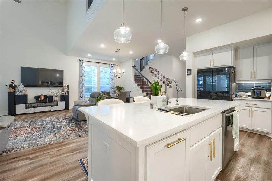 Kitchen with white cabinetry, sink, hanging light fixtures, light hardwood / wood-style flooring, and a kitchen island with sink