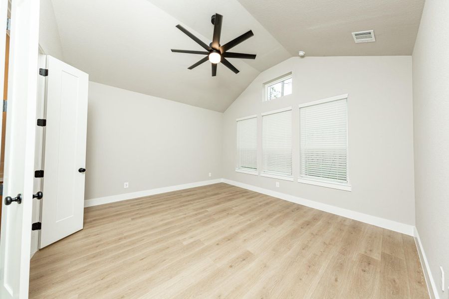 Relax and unwind after a long day in this impressive primary suite! This generously sized room offers the same wood-look flooring, neutral-toned paint, cathedral ceilings with a ceiling fan, and large windows for added comfort and tranquility.