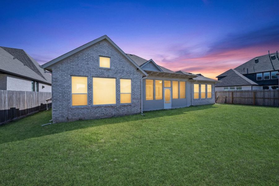 Striking rear elevation with expansive windows and covered patio—beautifully illuminated for evening ambiance.
