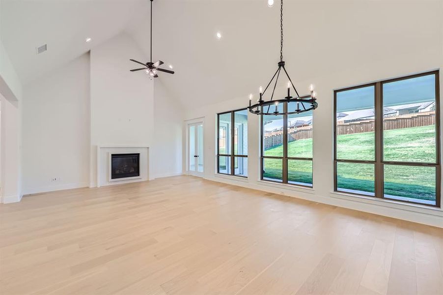 Unfurnished living room featuring high vaulted ceiling, ceiling fan with notable chandelier, and light wood-type flooring