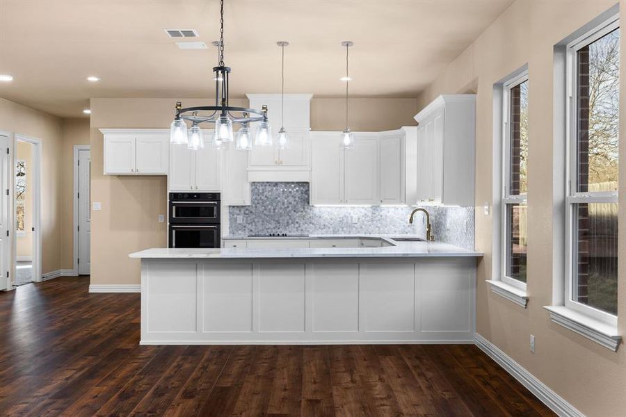 Kitchen with sink, white cabinetry, hanging light fixtures, decorative backsplash, and kitchen peninsula