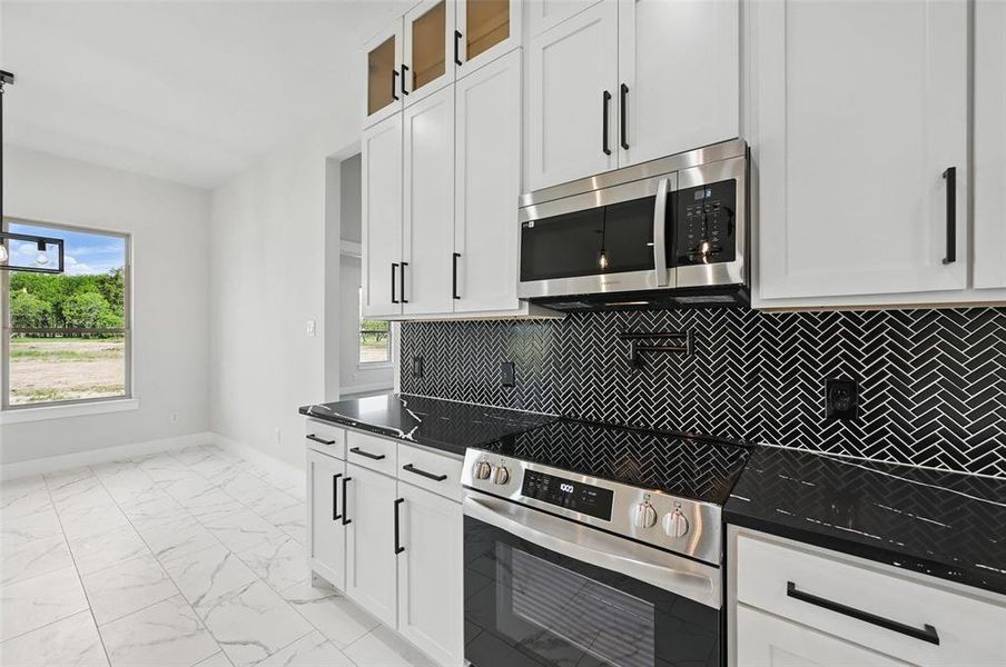 Kitchen with appliances with stainless steel finishes, light marble finish flooring, white cabinetry, and baseboards Kitchen with appliances with stainless steel finishes, light marble finish flooring, white cabinetry, and baseboards