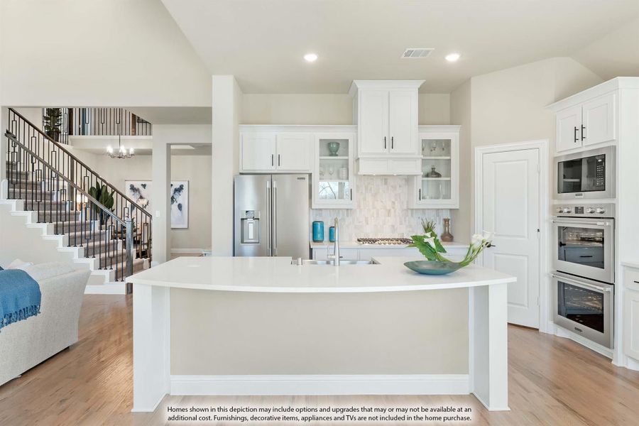 Open kitchen with white cabinets, large island, stainless steel appliances, and hardwood floors, open to staircase and living area. Open kitchen with white cabinets, large island, stainless steel appliances, and hardwood floors, open to staircase and living area.