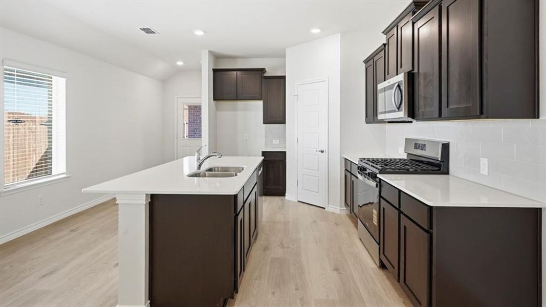 Kitchen featuring appliances with stainless steel finishes, light wood-style floors, light stone countertops, recessed lighting, and backsplash