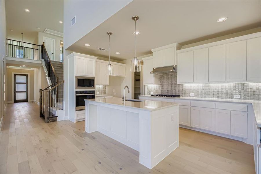 Kitchen featuring light wood-type flooring, pendant lighting, decorative backsplash, white cabinetry, and recessed lighting