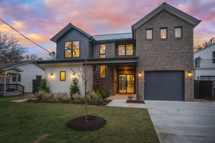 Modern home with brick siding, a standing seam roof, driveway, a front lawn, and a metal roof
