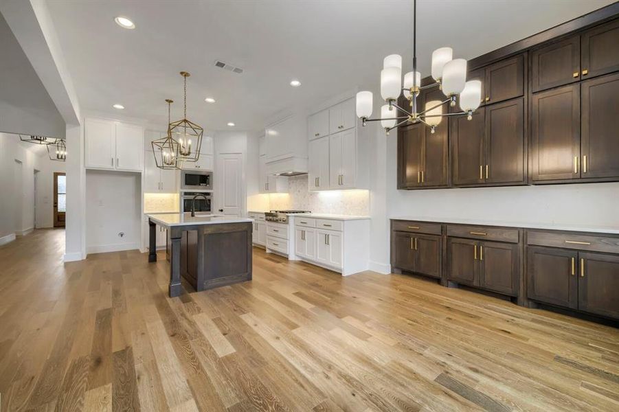 The open-concept kitchen features a large island with a sink, white cabinetry, integrated appliances, and light wood flooring