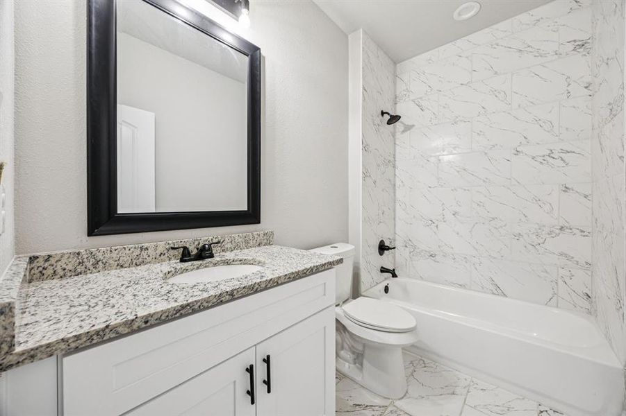 Full Bathroom off of the hallway featuring tub / shower combination, vanity with granite countertop, and light marble finish floors