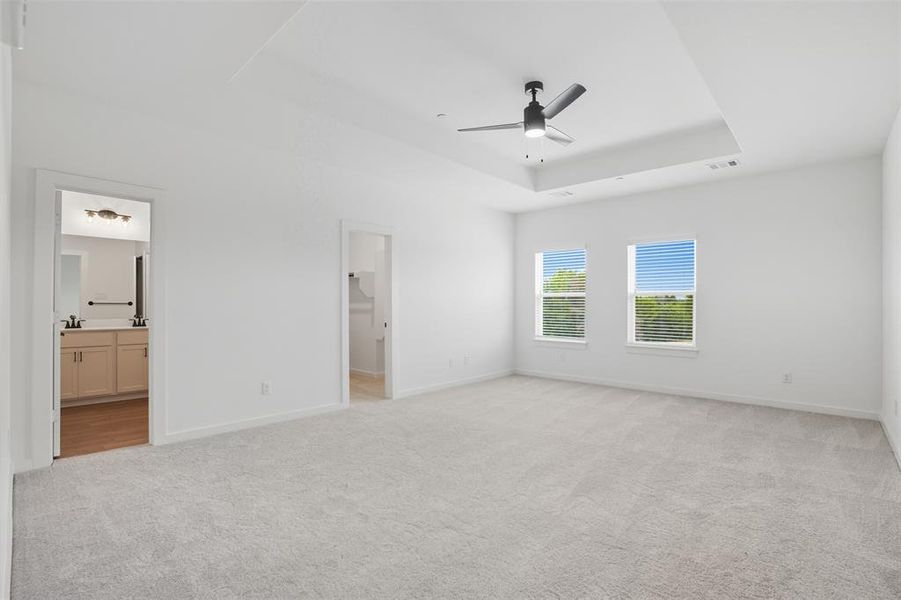 Unfurnished bedroom featuring a tray ceiling, light colored carpet, and ceiling fan Unfurnished bedroom featuring a tray ceiling, light colored carpet, and ceiling fan