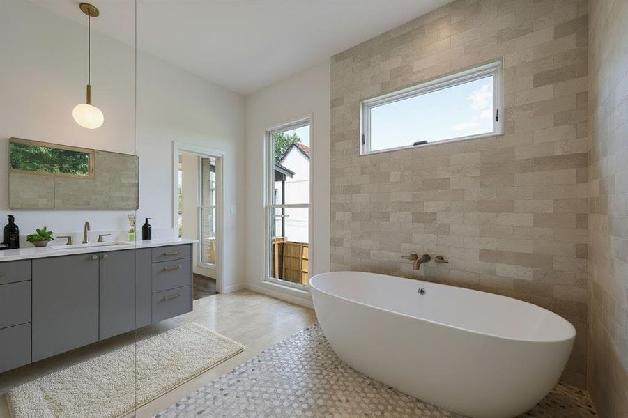 Bathroom with tile walls, a freestanding bath, vanity, plenty of natural light, and light wood-style flooring