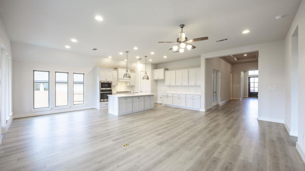 Kitchen featuring open floor plan, backsplash, a kitchen island with sink, light wood-type flooring, and ceiling fan Kitchen featuring open floor plan, backsplash, a kitchen island with sink, light wood-type flooring, and ceiling fan