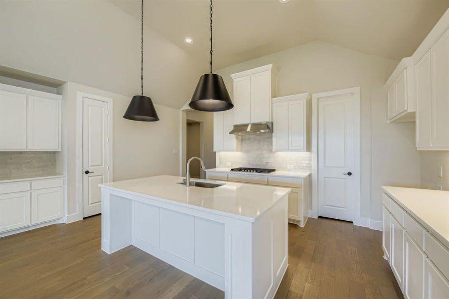 Kitchen with tasteful backsplash, lofted ceiling, white cabinetry, an island with sink, and light stone counters Kitchen with tasteful backsplash, lofted ceiling, white cabinetry, an island with sink, and light stone counters