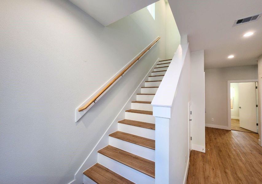 This photo showcases a bright, modern staircase with wooden steps and a sleek handrail, leading to the upper floor. The adjacent hallway features wood flooring and recessed lighting, creating a warm and inviting atmosphere. This photo showcases a bright, modern staircase with wooden steps and a sleek handrail, leading to the upper floor. The adjacent hallway features wood flooring and recessed lighting, creating a warm and inviting atmosphere.