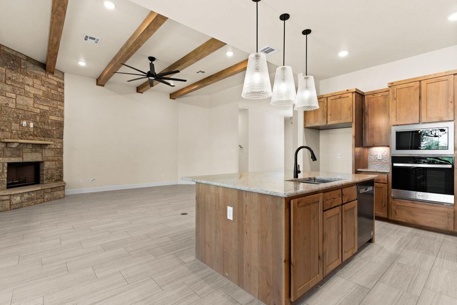 Kitchen featuring brown cabinetry, light stone counters, decorative light fixtures, a fireplace, and appliances with stainless steel finishes Kitchen featuring brown cabinetry, light stone counters, decorative light fixtures, a fireplace, and appliances with stainless steel finishes