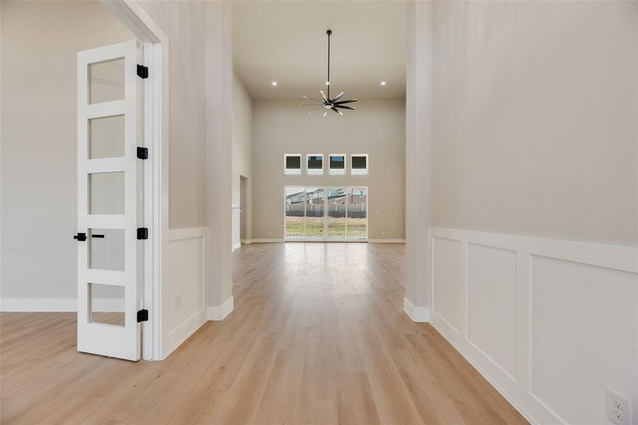 Hallway featuring light wood-type flooring, a high ceiling, a wainscoted wall, a decorative wall, and recessed lighting