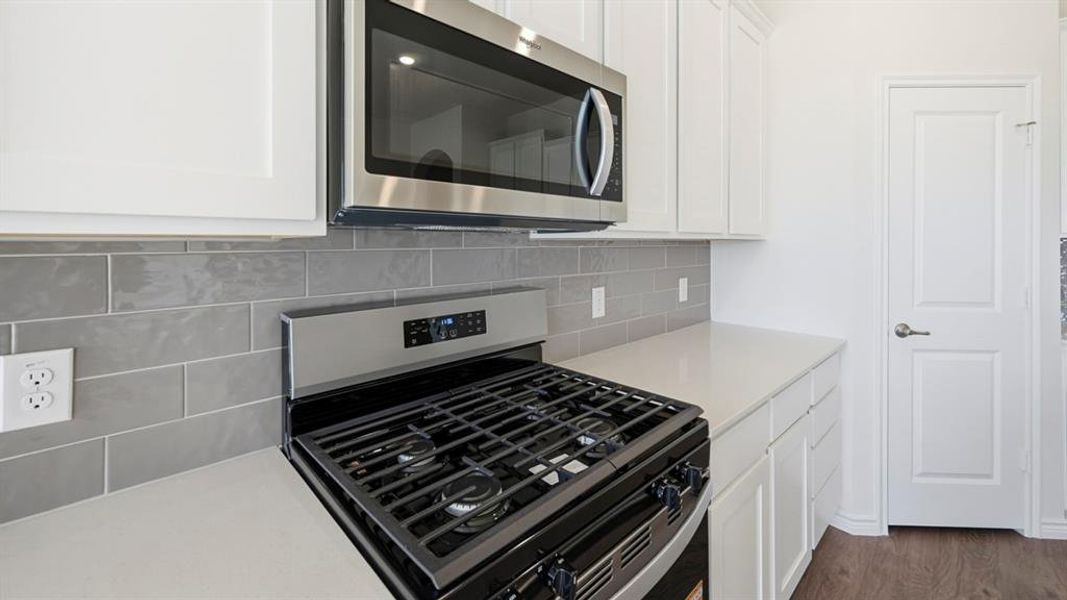 Stainless steel gas range with coordinating microwave, quartz countertops, and a gray subway tile backsplash