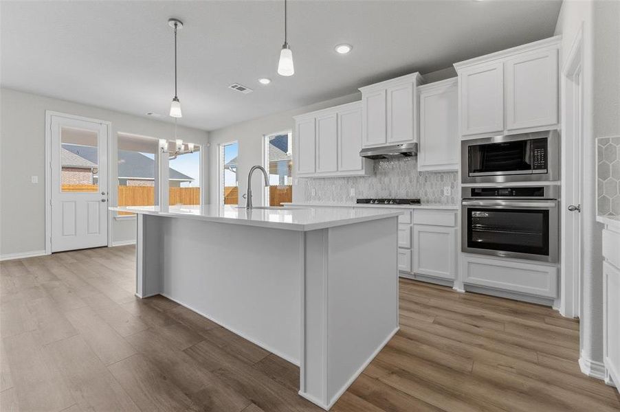 Kitchen with white cabinets, stainless steel appliances, decorative backsplash, and light wood-style floors