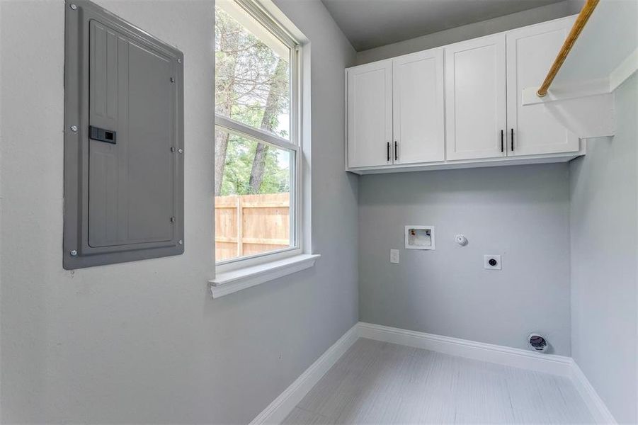 Clothes washing area featuring cabinets, electric panel, hookup for a gas dryer, hookup for a washing machine, and hookup for an electric dryer