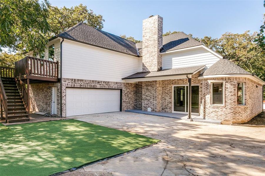 Rear view of property featuring a shingled roof, concrete driveway, stairs, a chimney, and brick siding