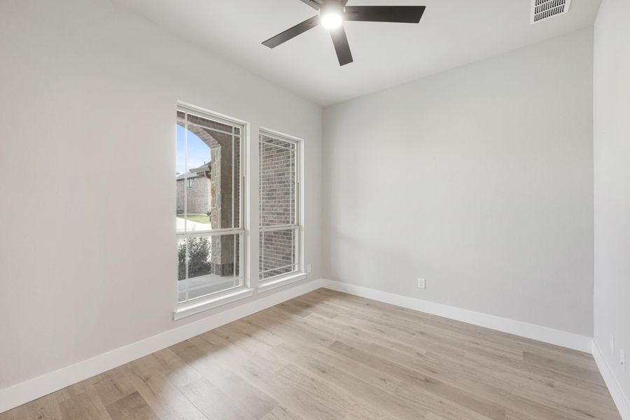 Empty room with light wood floors, ceiling fan, and two windows with exterior view