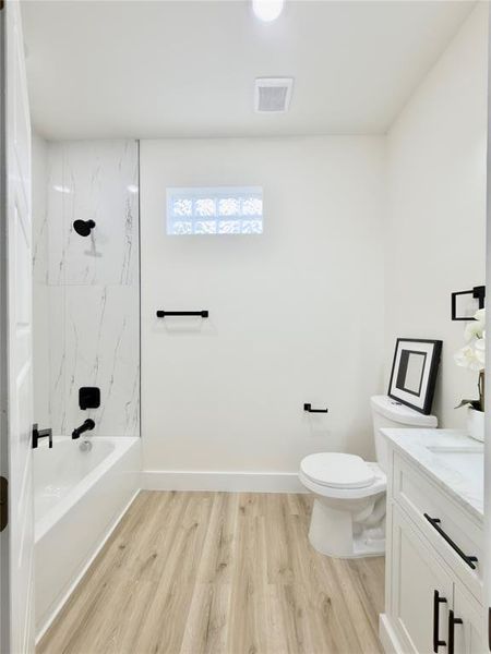 Bathroom featuring a bathtub with a tiled surround, wood-finish flooring, a white vanity with a countertop, and a glass block window