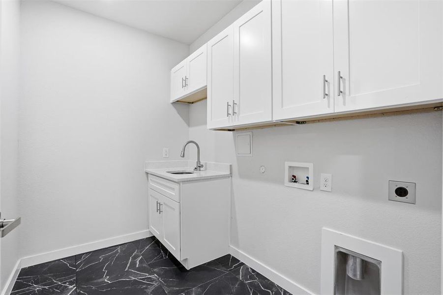 Utility room featuring white shaker cabinetry, an undermount sink with a gooseneck faucet, a light-toned countertop, and dark patterned floor tiles