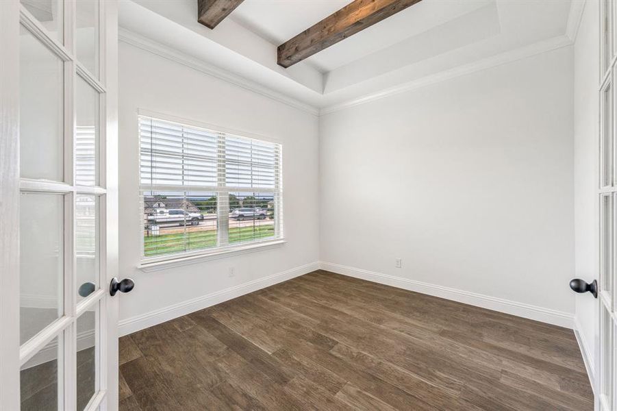 Empty room with crown molding, dark wood-type flooring, beamed ceiling, and a tray ceiling