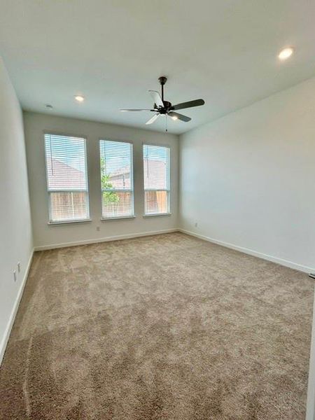 Spacious carpeted room featuring three vertical windows with blinds, a ceiling fan with integrated lighting, and recessed lighting