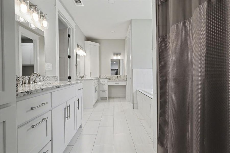 Spacious bathroom featuring white cabinetry with brushed nickel hardware, granite countertops, dual sinks, tile flooring, and a built-in soaking tub with subway tile surround
