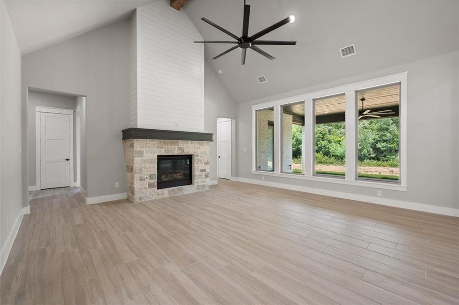 Spacious living area featuring a vaulted ceiling, wood-finish flooring, and a stone fireplace with a shiplap surround