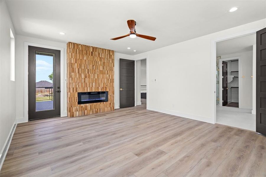 This inviting room features light wood-style flooring, a unique wood-paneled accent wall with an integrated fireplace, and a ceiling fan This inviting room features light wood-style flooring, a unique wood-paneled accent wall with an integrated fireplace, and a ceiling fan