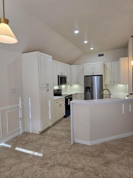 Kitchen featuring pendant lighting, stainless steel appliances, a peninsula, lofted ceiling, and white cabinets Kitchen featuring pendant lighting, stainless steel appliances, a peninsula, lofted ceiling, and white cabinets