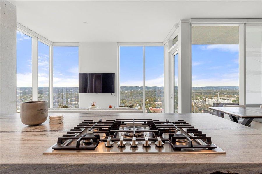 Chef’s island with Bosch gas cooktop overlooking the living area and sweeping Hill Country views, framed by floor-to-ceiling glass and direct terrace access.