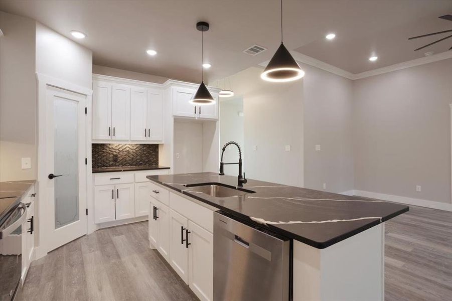 Kitchen featuring sink, white cabinetry, pendant lighting, stainless steel dishwasher, and a kitchen island with sink