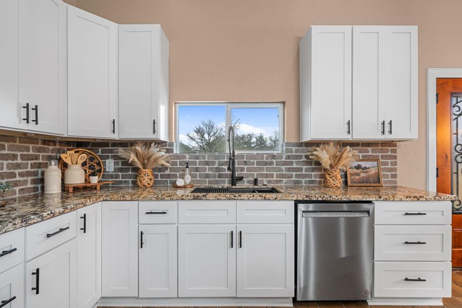 The brick-look backsplash adds a layer of timeless character, perfectly complementing the sleek stainless steel appliances and clean white shaker cabinetry.
