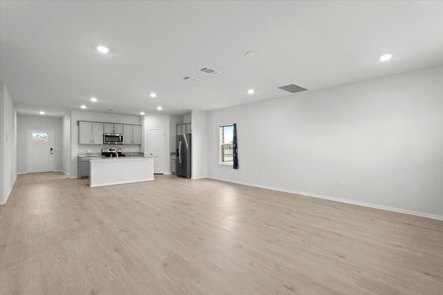 Open-concept living area with light wood-finish flooring, recessed lighting, and a kitchen featuring gray cabinetry, stainless steel appliances, and a central island with a countertop