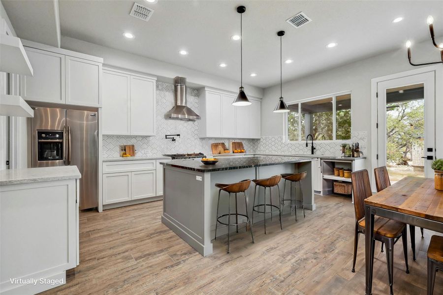 Kitchen with wall chimney range hood, visible vents, white cabinets, and stainless steel fridge with ice dispenser