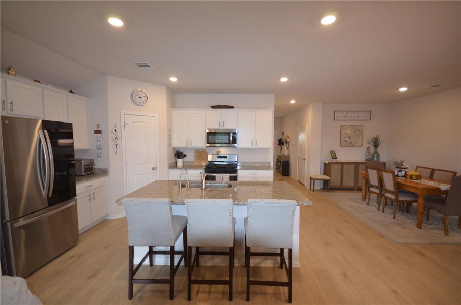 Kitchen with appliances with stainless steel finishes, a kitchen breakfast bar, light wood-style floors, white cabinetry, and recessed lighting Kitchen with appliances with stainless steel finishes, a kitchen breakfast bar, light wood-style floors, white cabinetry, and recessed lighting