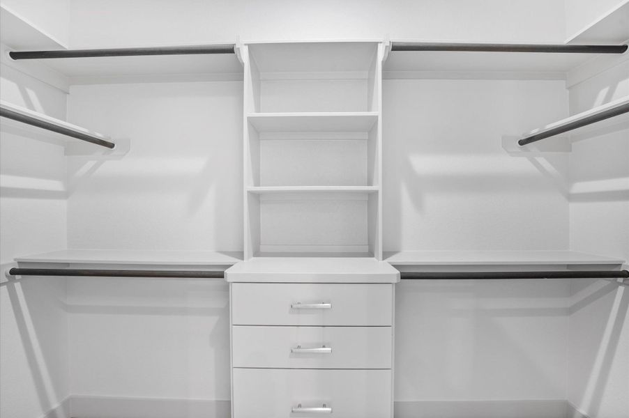 This photo shows a spacious and organized walk-in closet with multiple hanging rods, open shelves, and drawers, ideal for efficient clothing and accessory storage. This photo shows a spacious and organized walk-in closet with multiple hanging rods, open shelves, and drawers, ideal for efficient clothing and accessory storage.