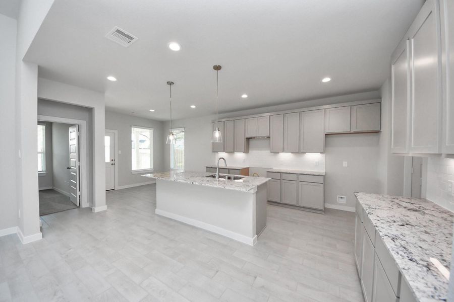 This generously spacious kitchen is a dream realized! With a massive granite island, high ceilings, soft close cabinets, granite countertops, stainless steel appliances, a sleek tile backsplash, recessed lighting, and an extended counter area, it offers both style and practicality. All this opens up to the expansive family room, creating a perfect hub for gatherings. Sample photo of completed home with similar floor plan. Actual colors and selections may vary.