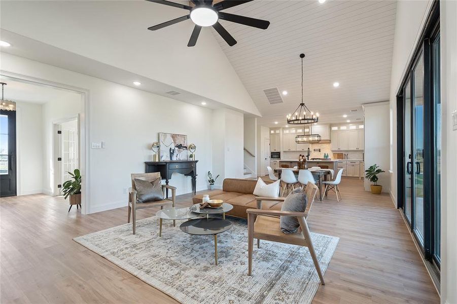 Living room featuring ceiling fan with notable chandelier, high vaulted ceiling, and light hardwood / wood-style flooring