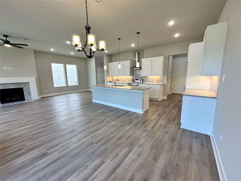 Kitchen with decorative light fixtures, ceiling fan with notable chandelier, wall chimney exhaust hood, white cabinets, and light wood-type flooring